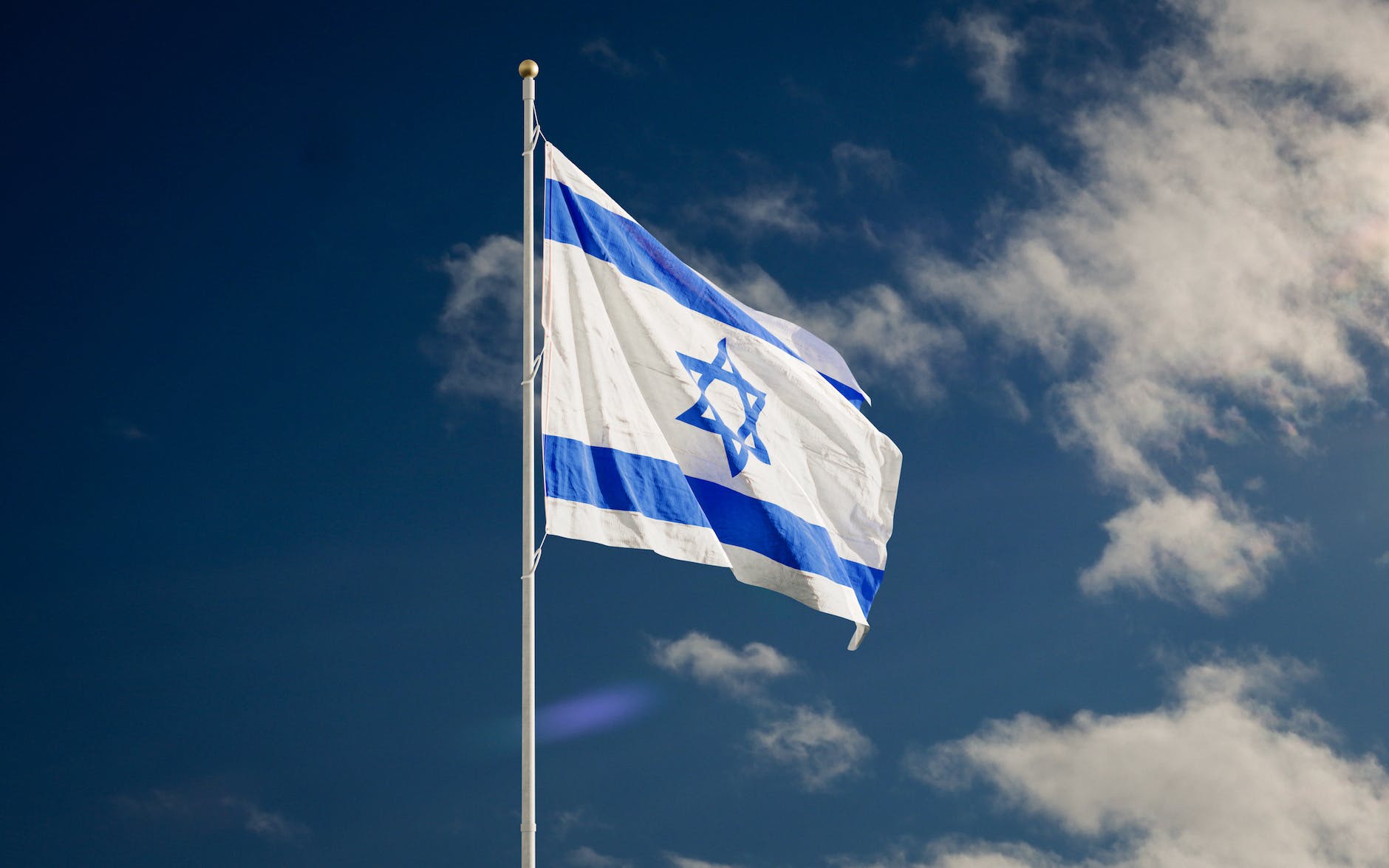 israel flag on a flagpole under the blue sky
