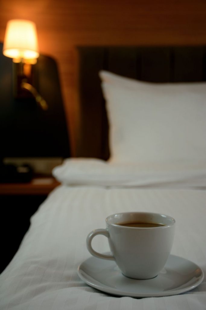 cup of coffee on white ceramic cup and saucer on bed