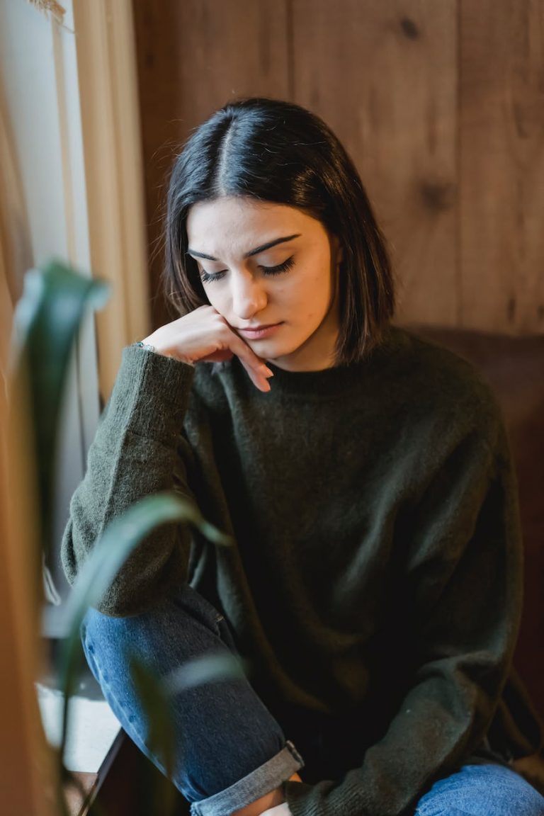 sad woman in casual wear sitting near window