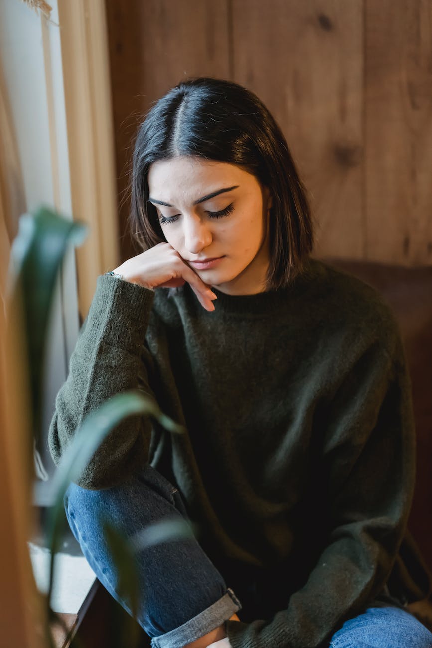 sad woman in casual wear sitting near window
