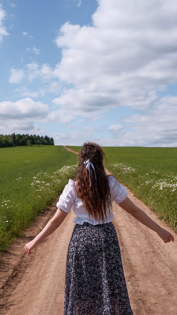 a back view of a woman in floral skirt standing between green grass field