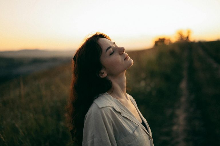 beautiful young woman standing in the meadow with eyes closed
