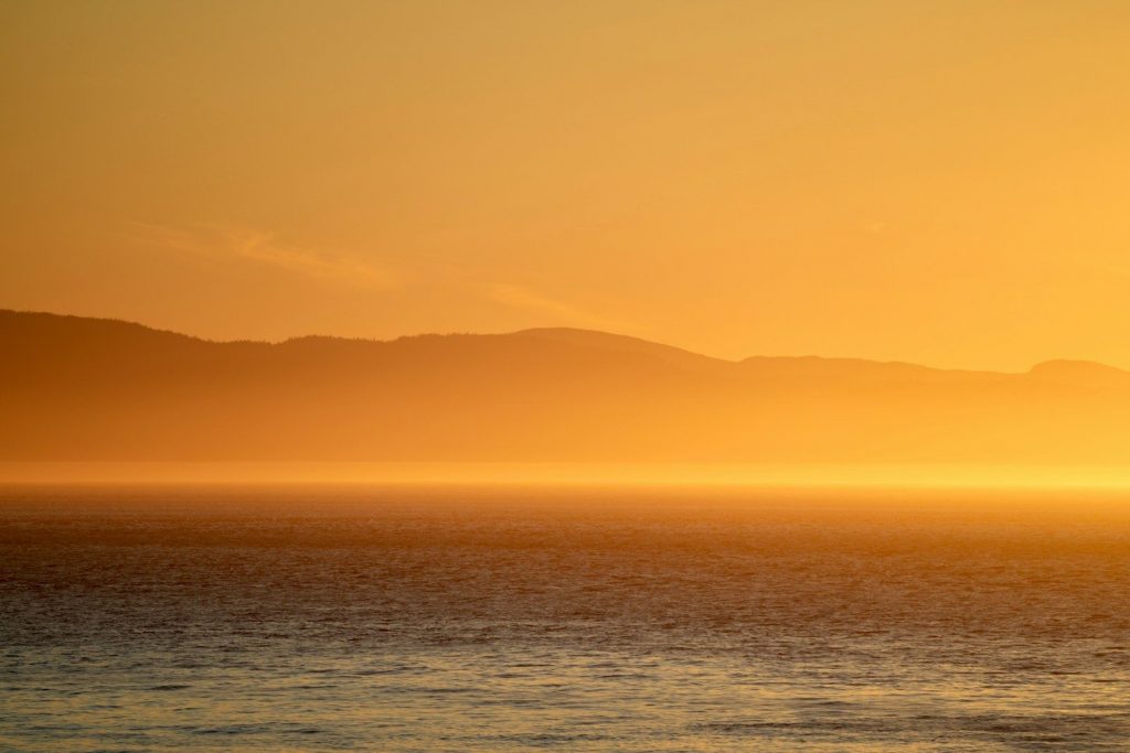 Golden sunset over ocean with distant mountains.