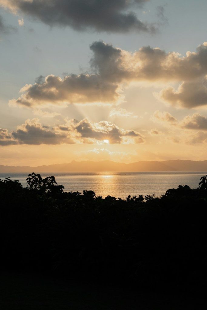 Low sun glowing behind clouds over a calm sea and distant mountain silhouettes